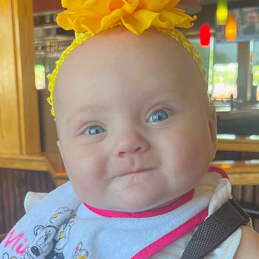 Reily is registered to the contest to win money with this photo: baby, bib, blue_eyes, child, colorful_lights, cute, date_overlay, digital_clock, face, happy, headband, high_chair, indoor, infant, portrait, restaurant, seatbelt, smile, wooden_furniture, yellow_flower