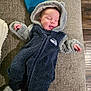 Asher is registered to the contest to win money with this photo: baby, infant, sleeping, onesie, hoodie, cozy, plush, couch, sofa, blanket, hat, tongue_out, hand, foot, face, human, peaceful, texture, wood_floor, sports_logo