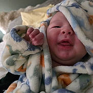 Asher is registered to the contest to win money with this photo: baby, newborn, blanket, hood, swaddle, cozy, face, tongue, chubby_cheeks, hand, fingers, indoor, couch, pillow, soft_texture, patterned_fabric, portrait, skin, smile, cute