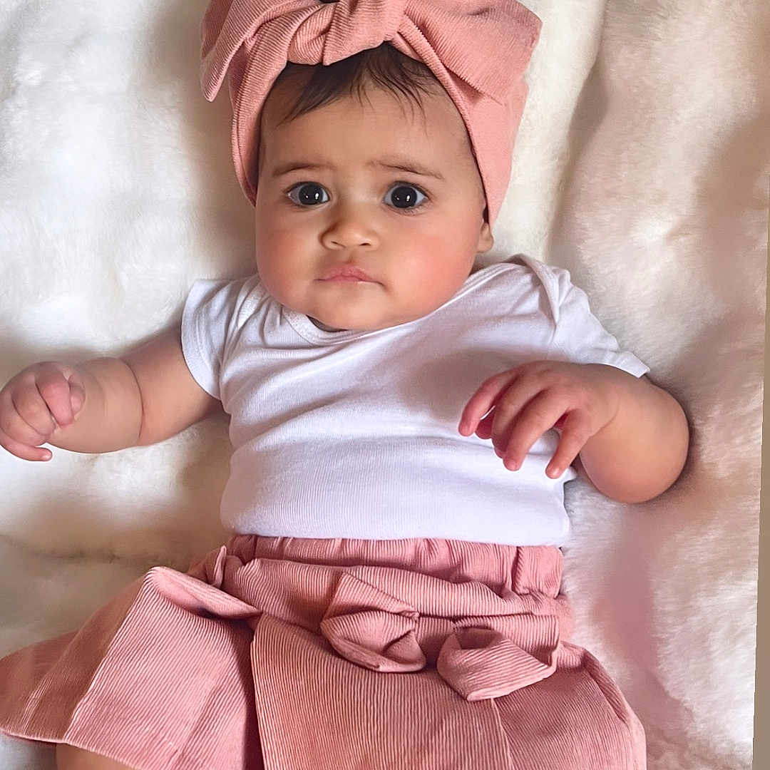 Sharlotte is registered to the contest to win money with this photo: baby, blanket, child, chubby_cheeks, cute, expression, fashion, footwear, hands, headband, indoors, infant, laying_down, pink_bow, portrait, skin, skirt, soft_texture, toddler, white_shirt