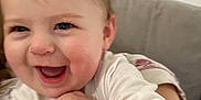 Amelia is registered to the contest to win money with this photo: baby, child, closeup, couch, cozy, cute, expression, face, hand, happy, human, indoor, infant, person, pink, portrait, skin, smiling, white_clothing, young_child