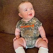 Paisley joined the competition — help win amazing prizes! baby, child, couch, clothing, camouflage, sitting, smiling, drool, white_socks, earrings, infant, happy, cute, indoor, person, portrait, texture, brown, onesie, furniture