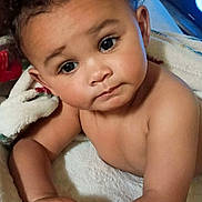 Nova is registered to the contest to win money with this photo: baby, child, infant, portrait, face, curly_hair, eyes, looking_at_camera, indoor, blanket, towel, sitting, lying_down, skin, arms, hands, close_up, soft_lighting, home, photography
