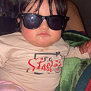 Natalia Julieth A O is registered to the contest to win money with this photo: baby, child, sunglasses, pink_pants, heart_pattern, cream_shirt, red_print, indoor, blanket, hand, person, face, hair, expressionless, casual_clothing, seated, closeup, infant, cute, cozy