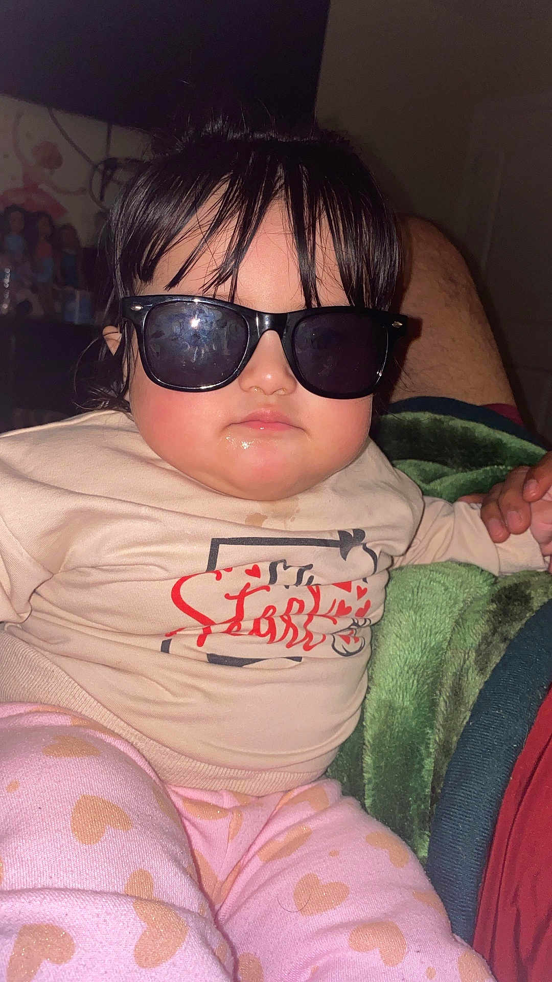 Natalia Julieth A O is registered to the contest to win money with this photo: baby, child, sunglasses, pink_pants, heart_pattern, cream_shirt, red_print, indoor, blanket, hand, person, face, hair, expressionless, casual_clothing, seated, closeup, infant, cute, cozy