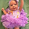 baby, infant, child, portrait, smiling, happy, bow, headband, tutu, dress, purple, floral, ruffles, fist, raised_arm, green_blanket, lying_down, indoor, colorful_clothing, celebration