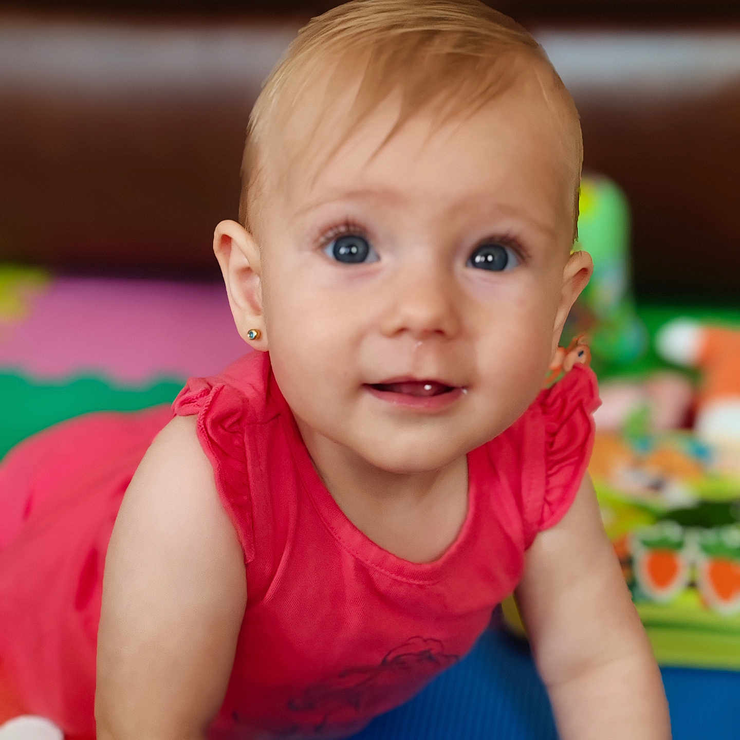 Karissa joined the competition — help win amazing prizes! baby, background, blue_eyes, child, closeup, colorful, crawling, cute, earrings, face, home, indoor, infant, person, pink_clothing, play_mat, smiling, soft_focus, toy, young_child