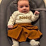 baby, infant, child, face, clothing, skirt, shirt, socks, baby_seat, cushion, indoor, floor, wooden_floor, expression, gaze, cute, small_hands, small_feet, portrait, comfort