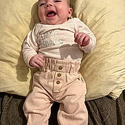 Inaya participe au concours pour gagner de l'argent avec cette photo : baby, smiling, infant, lying_down, pillow, cushion, pink_pants, corduroy, long_sleeve_shirt, text_on_clothing, striped_socks, happy, cute, child, indoor, soft_texture, cozy, clothing, person, portrait