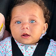 Kalaya is registered to the contest to win money with this photo: baby, blue_eyes, car_seat, child, curly_hair, face, infant, onesie, patterned_clothing, seatbelt, straps, close_up, portrait, expression, cute, young_child, skin, person, head, apparel
