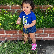 Eliza joined the competition — help win amazing prizes! toddler, child, flower, plants, grass, brick_wall, blue_shirt, pink_sneakers, outdoor, nature, greenery, young_child, cute, expression, standing, daylight, casual_clothing, person, small_plant, garden