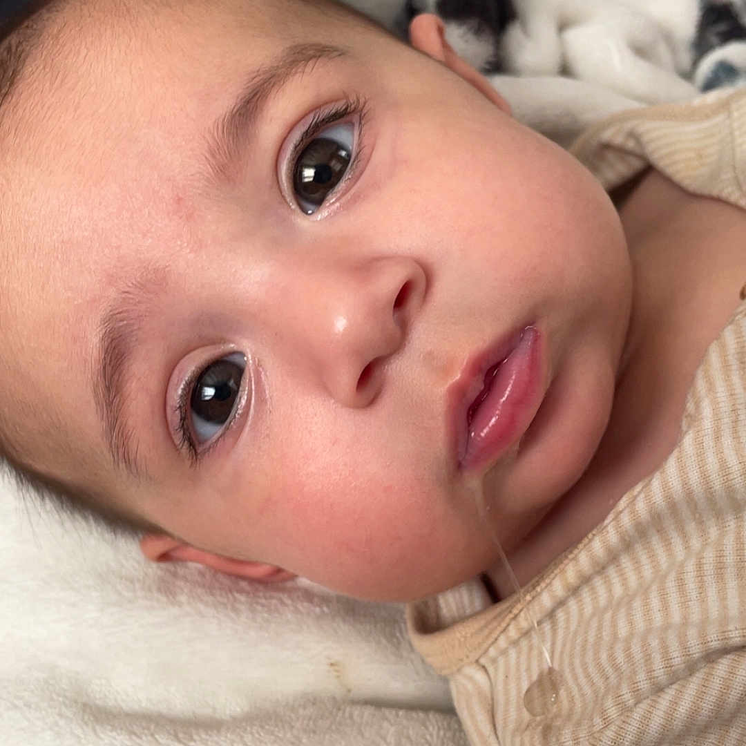 Lorelei is registered to the contest to win money with this photo: baby, blanket, closeup, cozy, cute, drool, expression, eyes, face, head, indoor, infant, lying_down, mouth, person, portrait, skin, soft_texture, striped_clothing, young_child