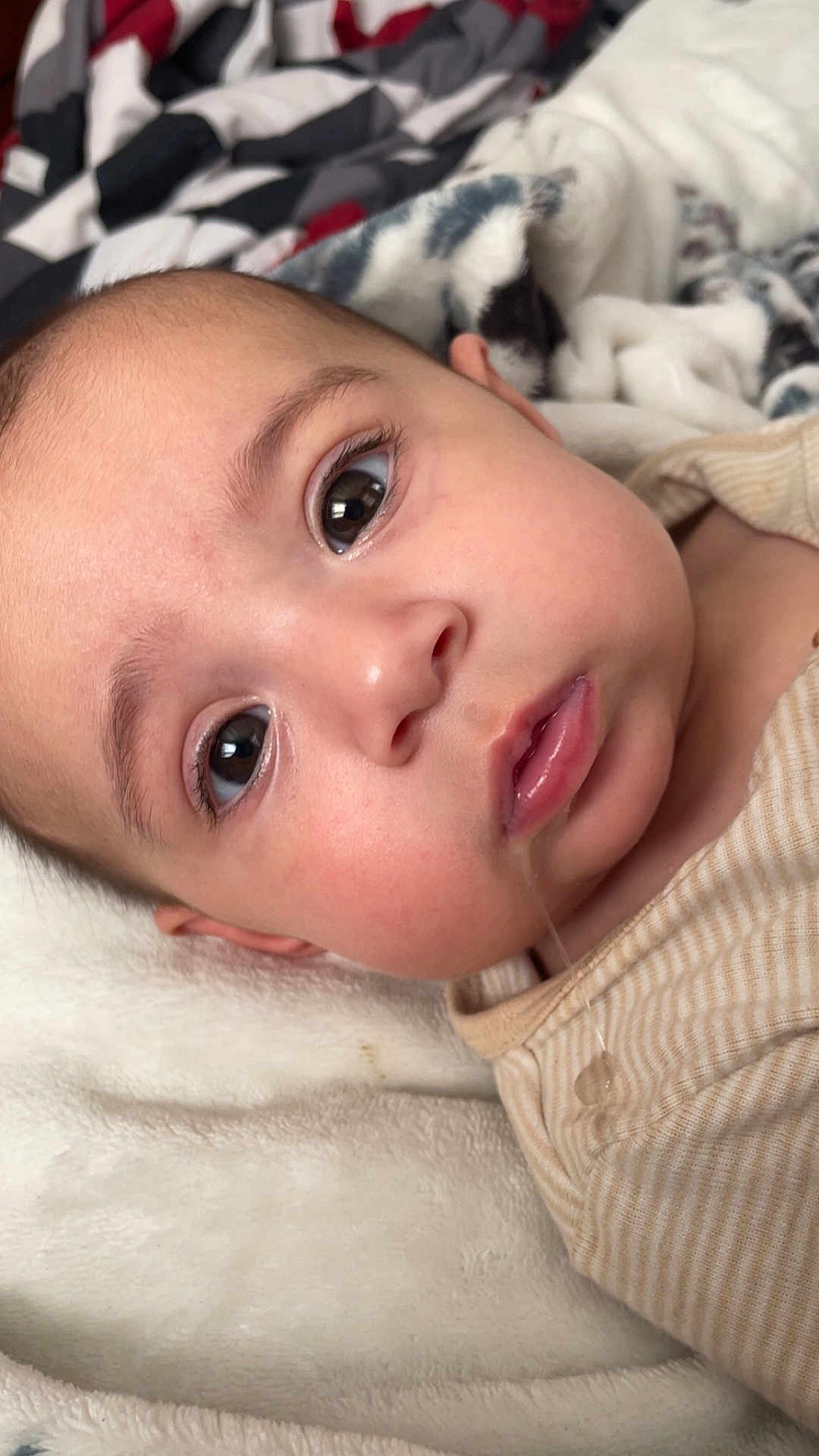 Lorelei is registered to the contest to win money with this photo: baby, closeup, drool, face, infant, lying_down, blanket, striped_clothing, soft_texture, cute, young_child, skin, eyes, mouth, head, cozy, portrait, indoor, person, expression