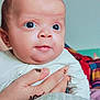 baby, infant, hand, henna, tattoo, face, eyes, skin, clothing, white_outfit, person, portrait, closeup, expression, curious, background, blurred, colorful, textile, indoor