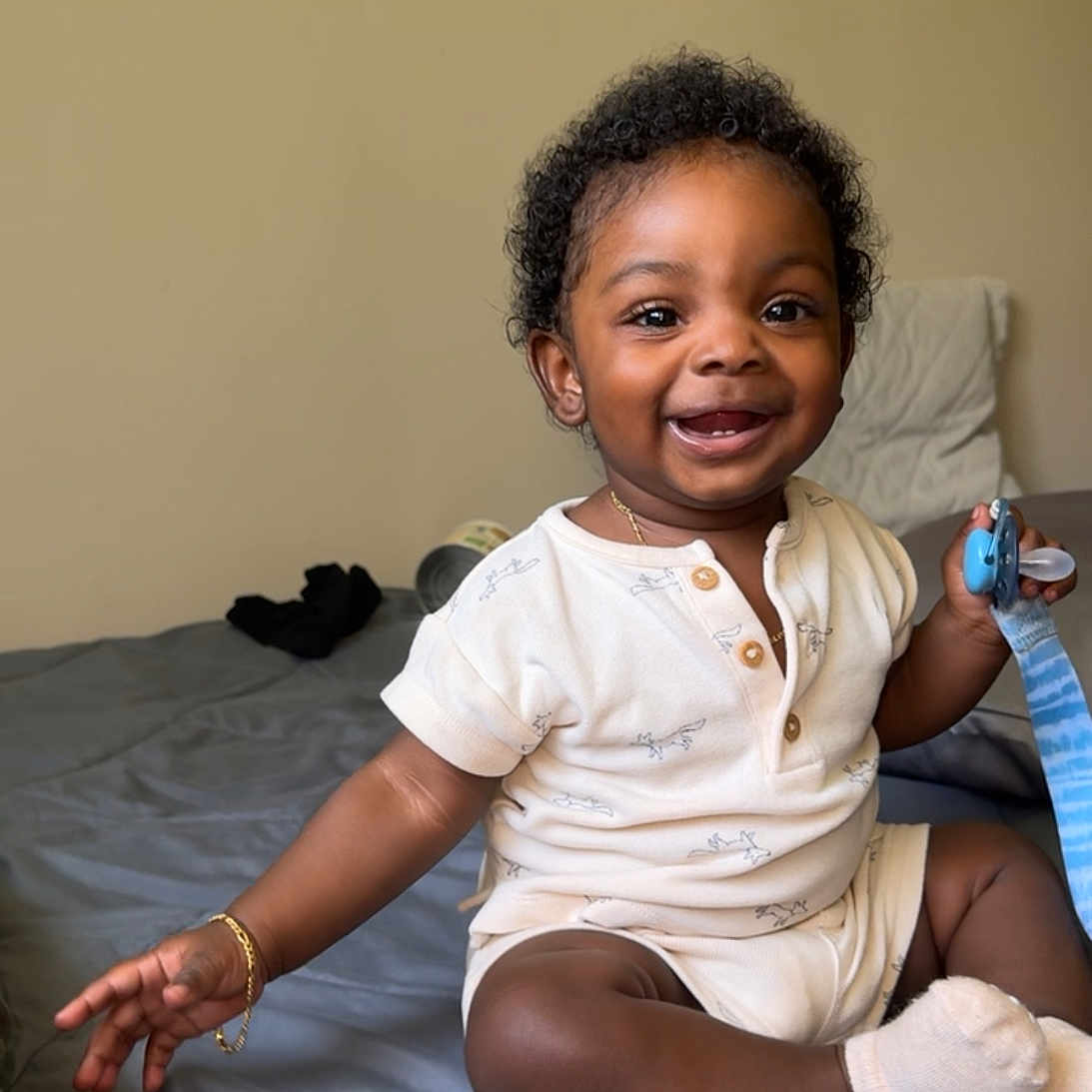 Josiah joined the competition — help win amazing prizes! baby, bed, blue, bracelet, child, clothing, comfort, curly_hair, cute, happy, indoor, infant, pacifier, person, room, sitting, skin, smiling, sock, toy