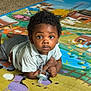 baby, child, indoor, playmat, toy, pacifier, curly_hair, carpet, floor, colorful, animal_print, infant, cute, lying_down, young_child, person, playtime, clothing, expression, home