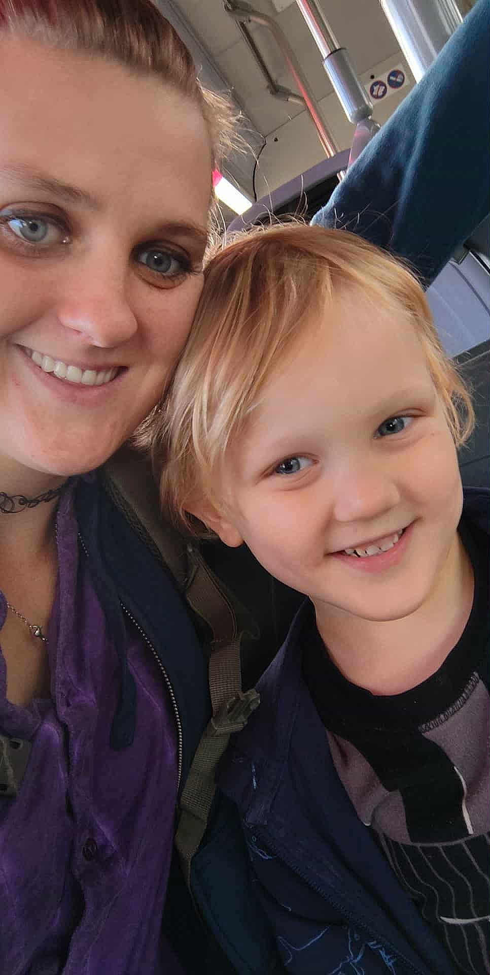 Colt is registered to the contest to win money with this photo: woman, child, smiling, portrait, face, person, public_transport, bus, seat, clothing, jacket, hair, blue_eyes, happy, closeup, indoors, casual, smile, young_child, parent