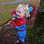 child, toddler, costume, spiderman, toy, blue, red, outdoor, autumn, leaves, tree, moss, grass, shoes, smiling, playful, pumpkins, cars, bush, nature