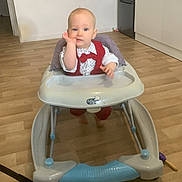 Lyam a rejoint le concours — aidez-le/la à gagner de superbes lots ! baby, baby_walker, child, indoor, floor, wooden_floor, kitchen, refrigerator, cabinet, furniture, person, clothing, red_outfit, white_shirt, sitting, face, hand, expression, home, cute