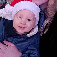 Lyam a rejoint le concours — aidez-le/la à gagner de superbes lots ! adult, baby, child, closeup, cozy, curly_hair, face, family, festive, hand, happy, holiday, indoor, jacket, person, portrait, santa_hat, smile, warm, winter_clothing