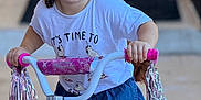 Jamilah is registered to the contest to win money with this photo: child, toddler, bicycle, pink, curly_hair, tshirt, denim_skirt, outdoor, toy, handlebars, foot, riding, play, happy, person, young_child, smile, daylight, cute, fun
