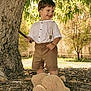 Aleks is registered to the contest to win money with this photo: child, toddler, smiling, outdoor, tree, stick, leafy_tree, teddy_bear_slippers, brown_shorts, white_shirt, sunlight, autumn, nature, playful, happy, grass, wood_chips, fence, background, daytime