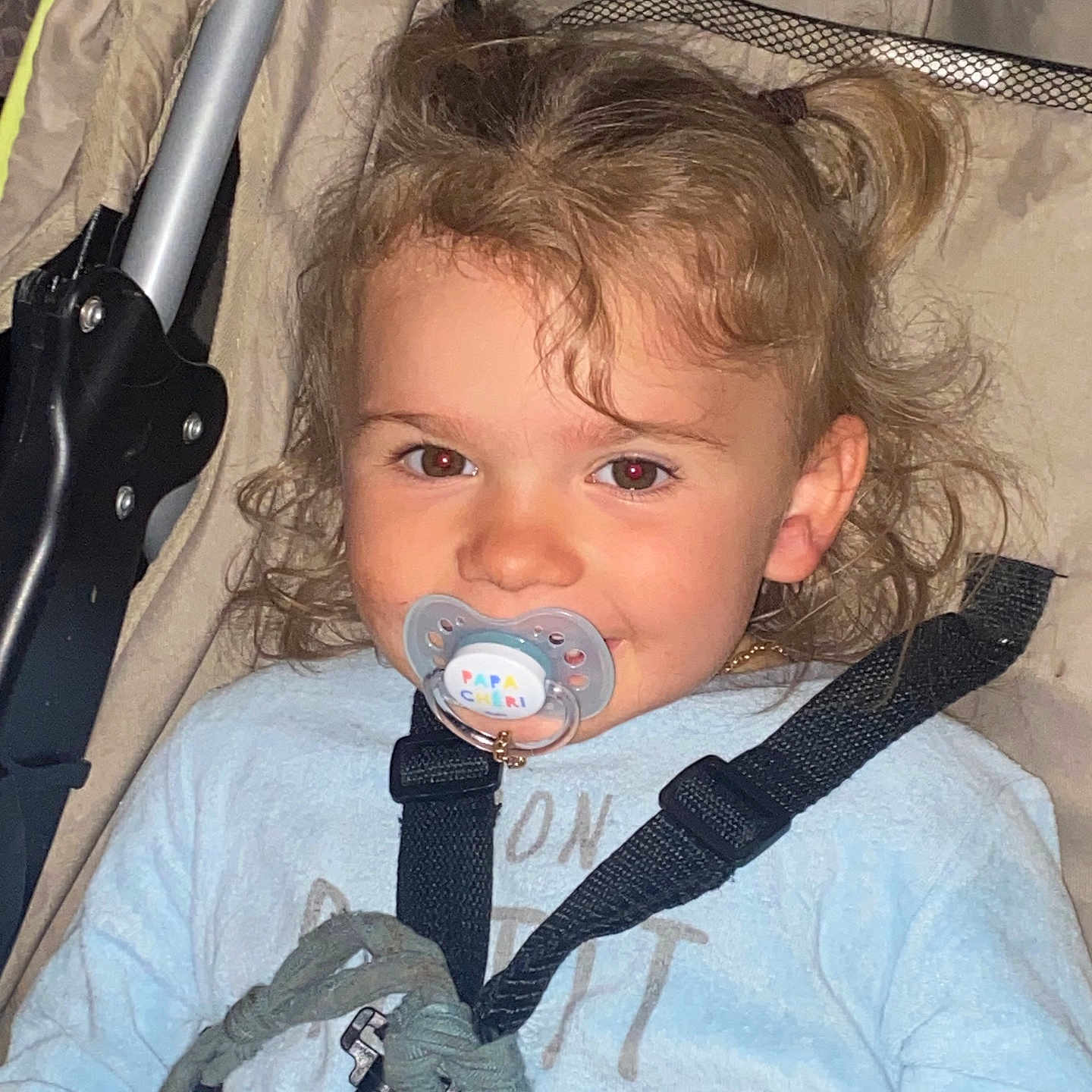 Nélia a rejoint le concours — aidez-le/la à gagner de superbes lots ! baby, child, closeup, clothing, curly_hair, cute, face, happy, harness, indoors, infant, light_blue_shirt, pacifier, person, seated, smiling, straps, stroller, toddler, young_child