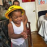 Ja'Hkai is registered to the contest to win money with this photo: bed, bedroom, chair, child, colorful, construction, gray_shorts, hands_clasped, happy, hard_hat, home, indoor, play, portrait, smiling, standing, toddler, wall_art, white_tank_top, wooden_floor