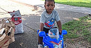 Ja'Hkai joined the competition — help win amazing prizes! benches, boy, braids, charcoal_bag, child, grass, gray_shirt, grocery_bags, outdoor, park, playground, portrait, ride_on_toy, sidewalk, sitting, sneakers, sunlight, toddler, toy_motorcycle, trees