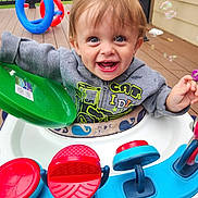 Daniel is registered to the contest to win money with this photo: toddler, child, baby, smiling, happy, blue_eyes, activity_walker, toys, bubbles, outdoor, deck, play, colorful, clothing, jacket, face, hands, fun, joy, person