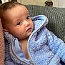 baby, child, blue_jacket, fluffy_clothing, indoor, couch, cushion, face, head, person, portrait, young_child, soft_texture, curious, seated, warm_clothing, human, infant, closeup, relaxed