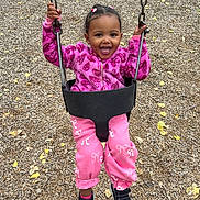 Zahara is registered to the contest to win money with this photo: child, toddler, swing, playground, pink_clothing, jacket, pants, shoes, smiling, happy, outdoor, woodchips, chains, play, fun, young_child, hair_bows, black_shoes, casual, daylight