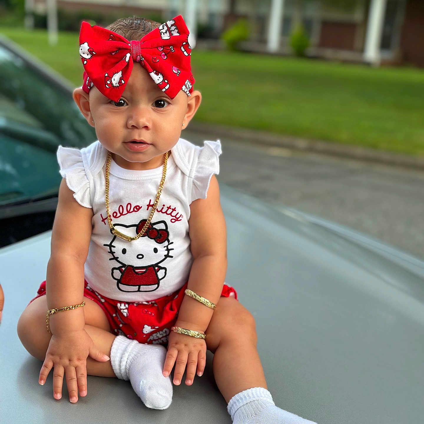 Ayla Ladale is registered to the contest to win money with this photo: accessories, baby, bow, bracelets, car_hood, child, cute, girl, greenery, hello_kitty, jewelry, necklace, outdoor, portrait, red_bow, shorts, sitting, suburban, tank_top, white_socks