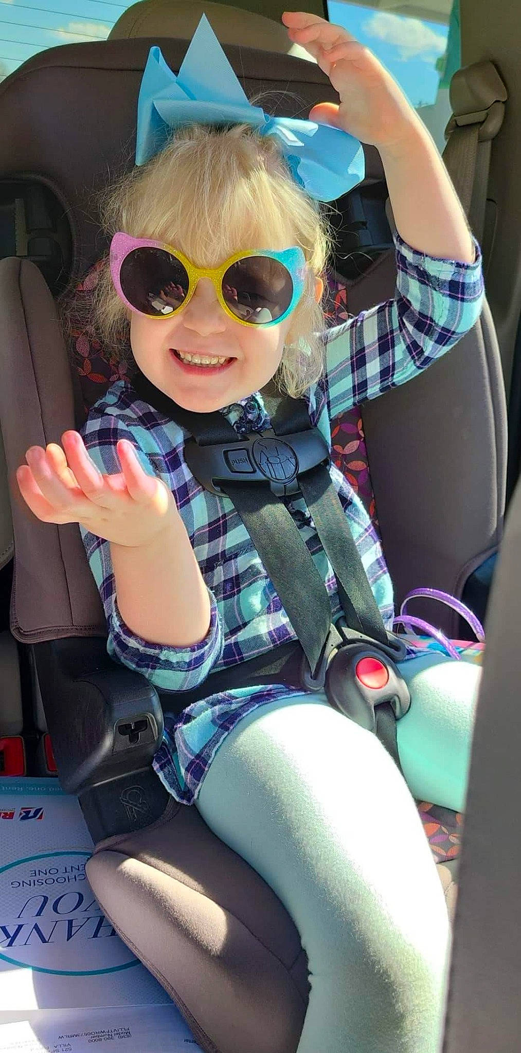 Ariah is registered to the contest to win money with this photo: arm, automotive_design, car_seat, eyewear, fun, glasses, goggles, hand, happy, joy, leg, motor_vehicle, person, personal_protective_equipment, plaid, smile, steering_wheel, sunglasses, thigh, toddler