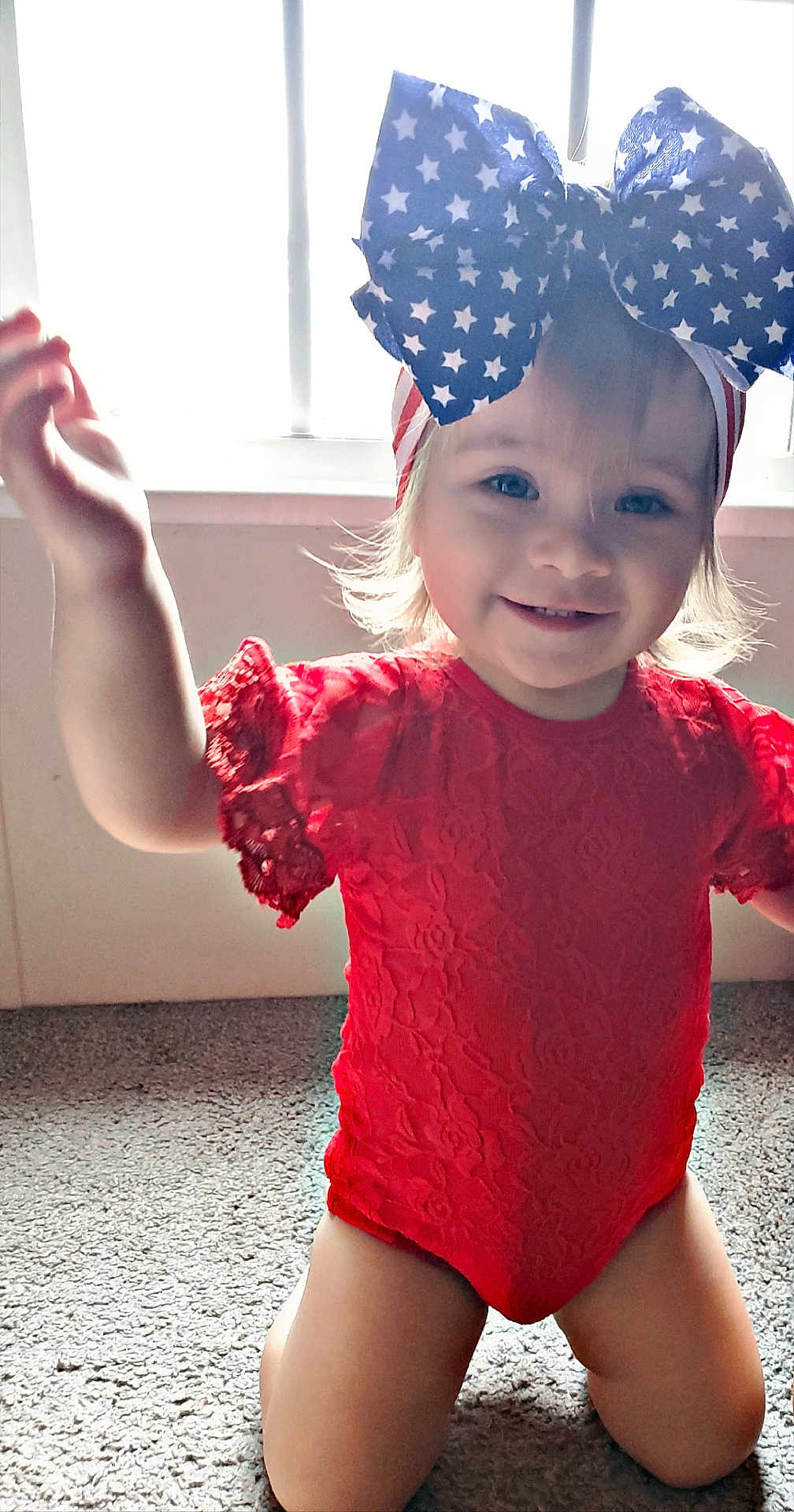 Mary is registered to the contest to win money with this photo: toddler, child, smiling, red_clothing, blue_bow, stars_pattern, headband, kneeling, carpet, indoor, window, natural_light, happy, cute, portrait, baby, person, face, young_child, playful