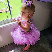 Mary is registered to the contest to win money with this photo: child, toddler, dress, purple, bow, window, carpet, barefoot, indoor, girl, standing, curtain, light, sunlight, looking_out, floor, person, cute, decor, toy