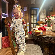 Madilynn is registered to the contest to win money with this photo: toddler, child, pajamas, chair, wooden_furniture, snack, smile, indoor, holiday_decorations, christmas_tree, table, pacifier, food, wood_floor, cushion, happy, person, home, lighting, cozy
