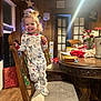 toddler, child, pajamas, chair, wooden_furniture, snack, smile, indoor, holiday_decorations, christmas_tree, table, pacifier, food, wood_floor, cushion, happy, person, home, lighting, cozy