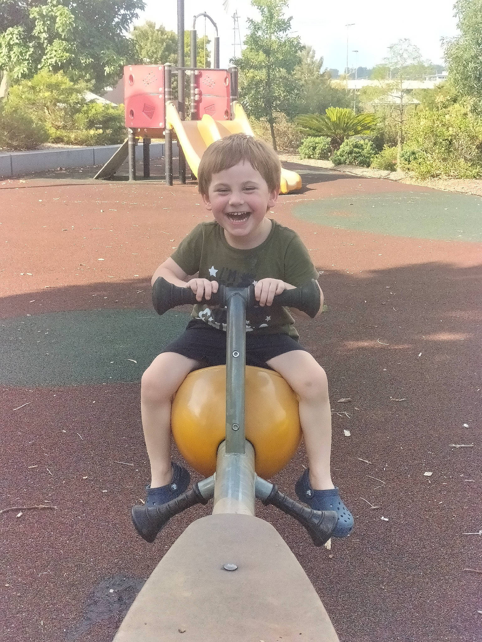 Izaiah joined the competition — help win amazing prizes! asphalt, baby, city, fun, grass, human_leg, joy, knee, leisure, outdoor_play_equipment, person, plant, playground, recreation, shorts, sitting, sky, smile, thigh, toddler