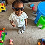 Kydorris is registered to the contest to win money with this photo: toddler, child, sunglasses, white_tshirt, gray_shorts, indoor, carpet, toy, playroom, colorful, green_chair, blue_table, sneaker, plastic_toy, basket, storage_drawers, smiling, standing, person, happy