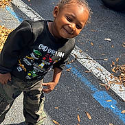 Kydorris joined the competition — help win amazing prizes! child, smiling, outdoor, parking_lot, asphalt, leaves, sweatshirt, camouflage_pants, sneakers, sunlight, playful, vehicle_prints, young_child, casual_clothing, person, daylight, happy, boy, standing, leaning