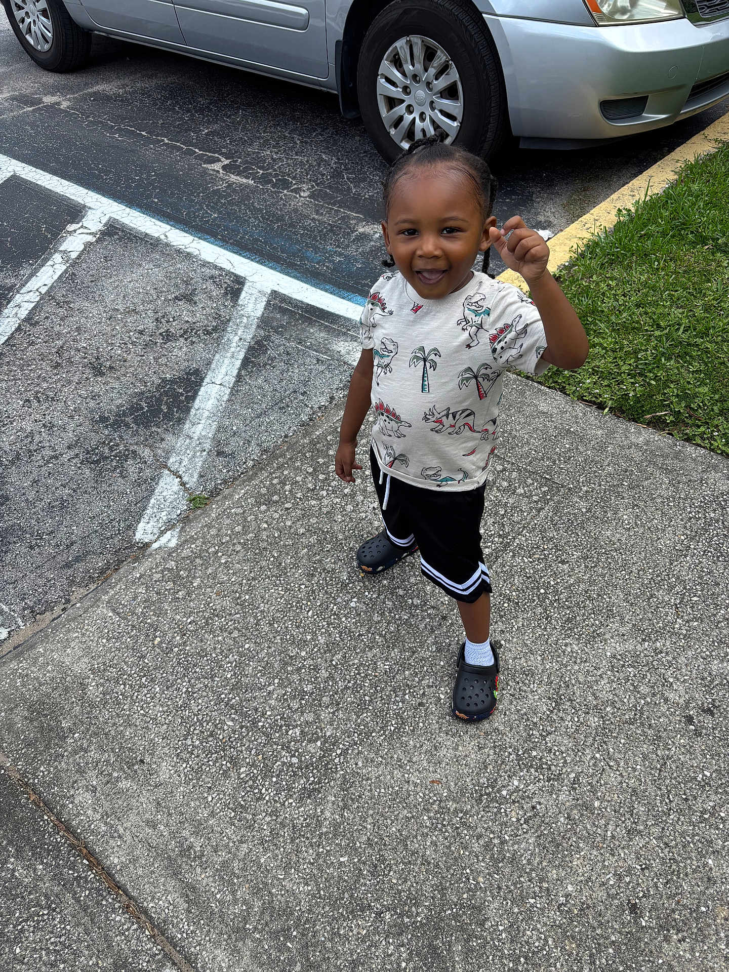 Kydorris joined the competition — help win amazing prizes! toddler, child, outdoor, sidewalk, parking_lot, car, grass, dinosaur_print, shirt, shorts, crocs, white_socks, smiling, happy, standing, asphalt, curb, hair_braids, casual_clothing, summer