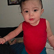 Genesis joined the competition — help win amazing prizes! toddler, child, baby, portrait, indoor, sitting, standing, red_shirt, pigtails, dark_hair, brown_eyes, facial_expression, looking_at_camera, home, bedroom, bed, blanket, framed_picture, close_up, family_photo