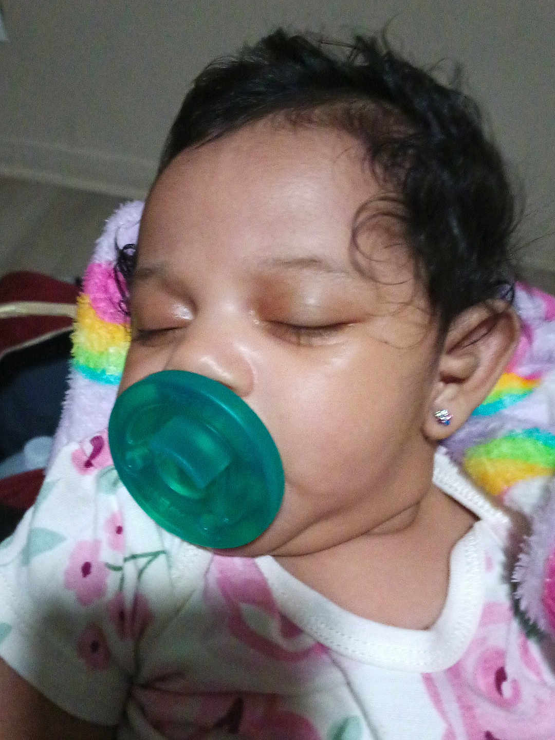 Mulaii is registered to the contest to win money with this photo: baby, sleeping, pacifier, curly_hair, earring, floral_clothing, blanket, closeup, infant, child, peaceful, face, indoors, cute, portrait, resting, soft_lighting, young_child, head, skin