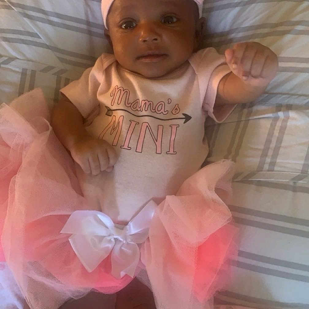 Judea is registered to the contest to win money with this photo: baby, blanket, booties, child, clothing, cute, flower, headband, indoors, infant, lying_down, person, pillow, pink, portrait, smiling, soft, striped, toddler, tutu