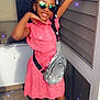 child, girl, smiling, posing, pink_dress, braids, white_beads, sunglasses, heart_shaped, silver_bag, sandals, outdoor, door, concrete_floor, wall, sunlight, shadow, happy, fashion, sparkles