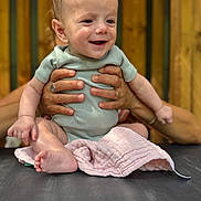 Livio participe au concours pour gagner de l'argent avec cette photo : baby, child, cute, face, hands, happy, holding, human, indoors, infant, onesie, person, pink_cloth, portrait, sitting, skin, smiling, table, wooden_background, young