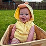 Cody is registered to the contest to win money with this photo: baby, child, basket, yellow_hoodie, duck_costume, grass, outdoor, smiling, happy, cute, face, person, garden, fence, spring, plush, striped_pants, blue_eyes, sunlight, nature
