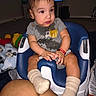 baby, child, infant, sitting, baby_seat, gray_shirt, socks, indoor, television, toy, floor, carpet, person, cute, expression, clothing, legs, hand, face, hair
