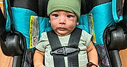 Hector is registered to the contest to win money with this photo: baby, car_seat, child, closeup, clothing, cute, expression, face, green_hat, green_socks, headwear, indoors, infant, person, portrait, safety, seatbelt, sitting, straps, wooden_floor